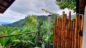 Vista da un balcone con una recinzione in bambù, vegetazione lussureggiante e un paesaggio montuoso sullo sfondo.