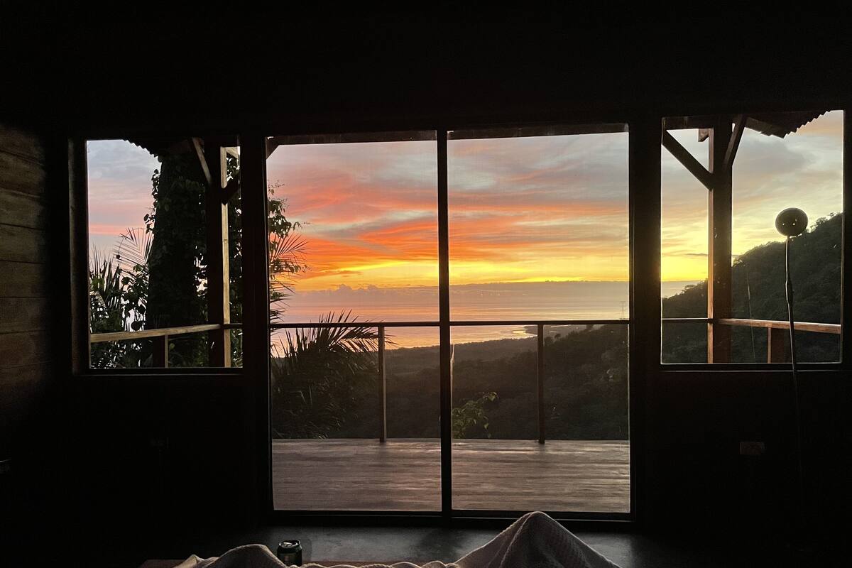 Una habitación con un amplio ventanal con vistas a un atardecer.