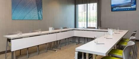 A conference room with a long white table, multiple chairs, and a large screen on the wall.