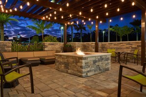 An outdoor patio with stone seating, a fire feature, and string lights. - SpringHill Suites by Marriott Fort Myers Estero (Estero)