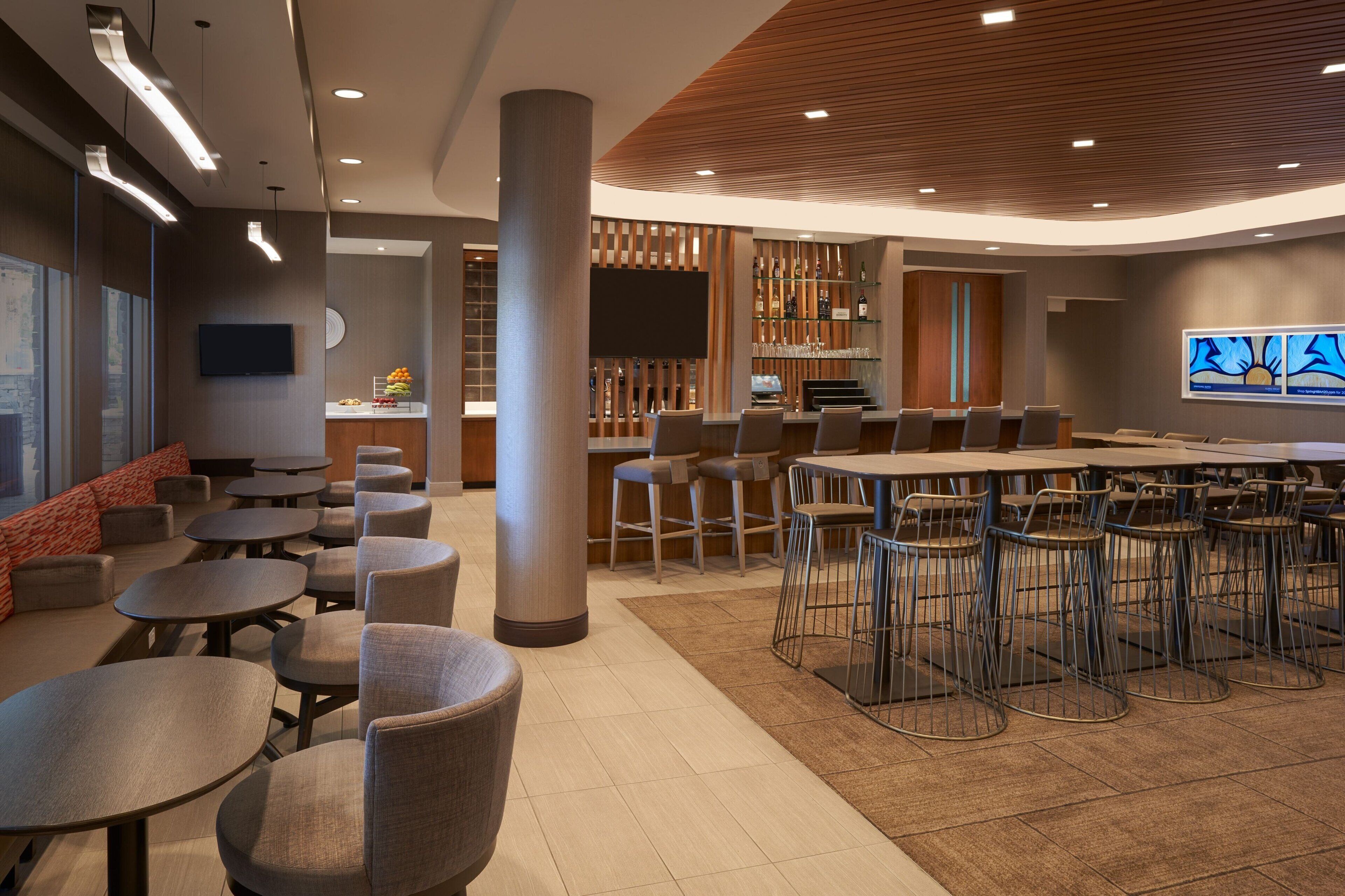 Un espace de détente moderne avec des tables rondes, des sièges de bar et un écran de télévision.