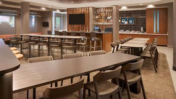 Een moderne hotellobby met verschillende eetgedeeltes, een bar en een zithoek met een groot scherm.