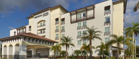 A multi-story hotel with a covered entrance, palm trees, and a clear sky.