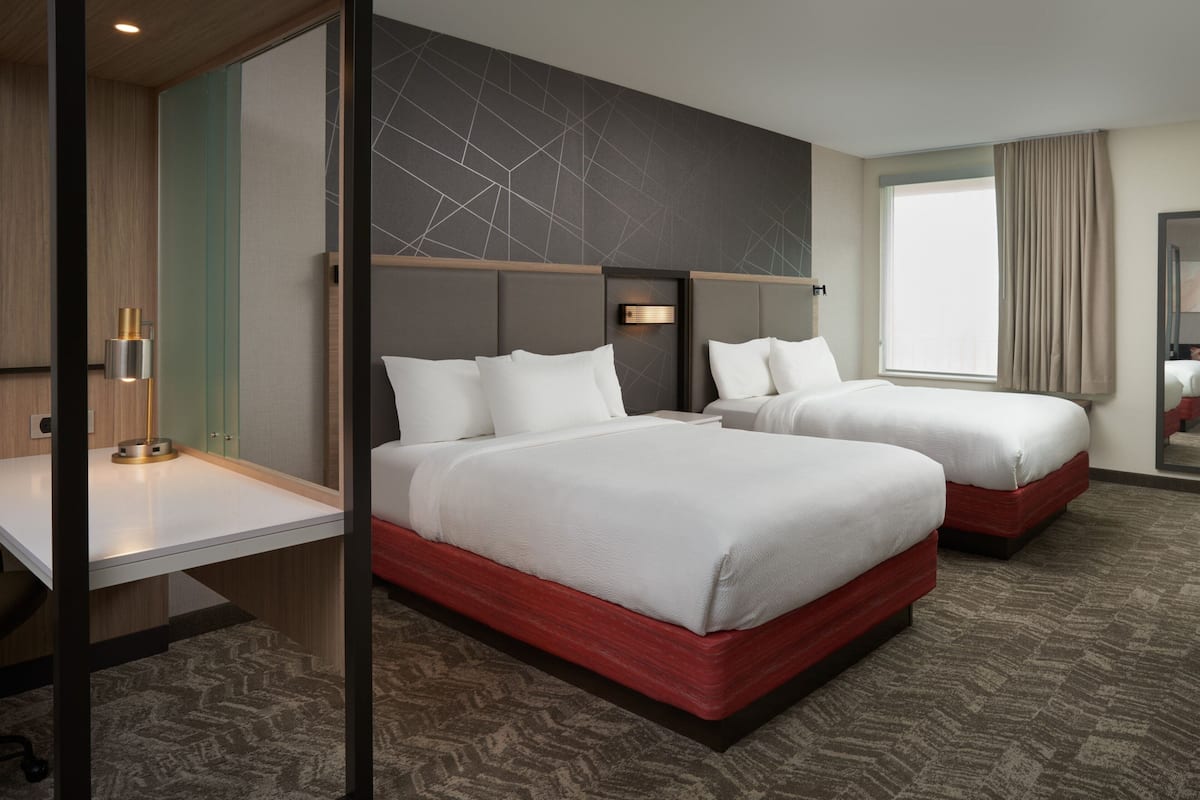 A hotel room with two beds, a desk, and a large window with curtains.