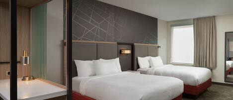 A hotel room with two beds, a desk, and a large window with curtains.