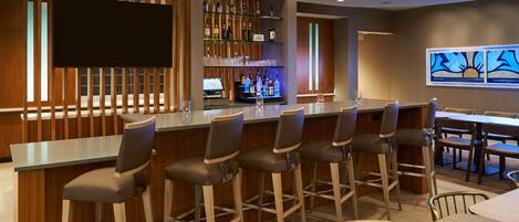 A bar area with a long counter, multiple bar stools, a television screen, and a wine rack with bottles.