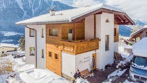 A mountain cabin with a wooden balcony, a stone fireplace, and a view of snow-covered mountains.