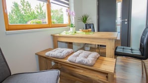A modern room with a wooden table, two benches, a potted plant, and a view of greenery outside.