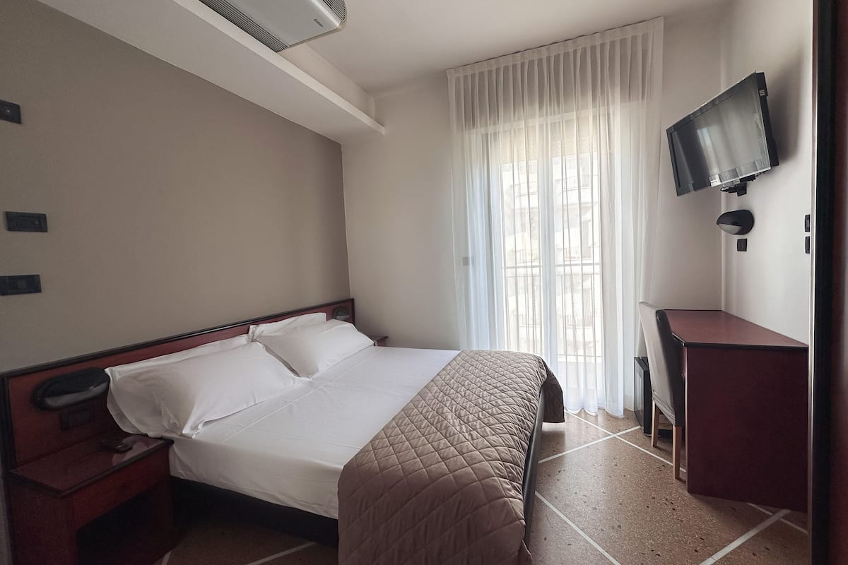 A hotel room with a bed, a desk, a television, and a window with curtains.
