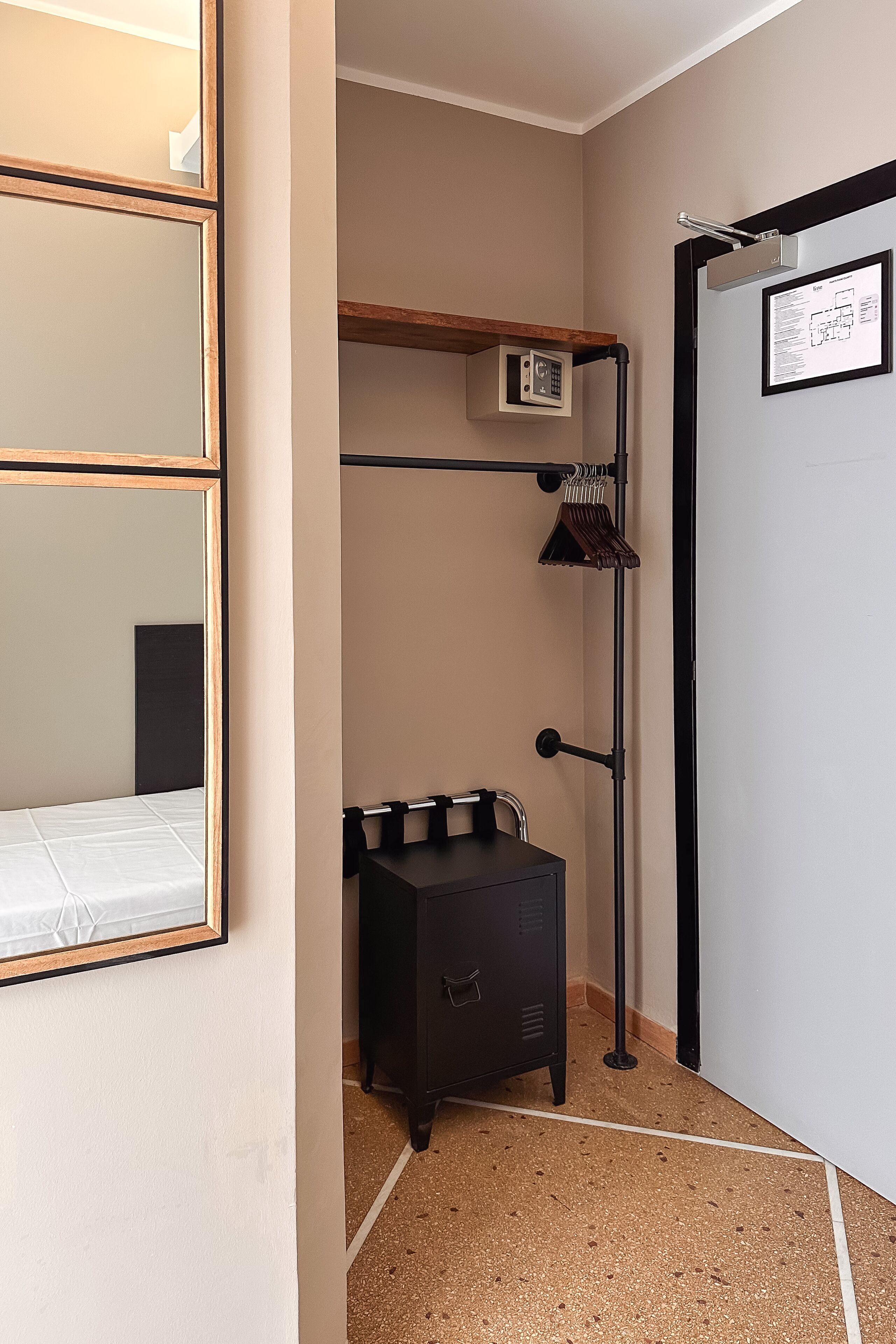A compact room with a bed, a small dresser, a mirror, a coat rack, and a door with a framed picture.