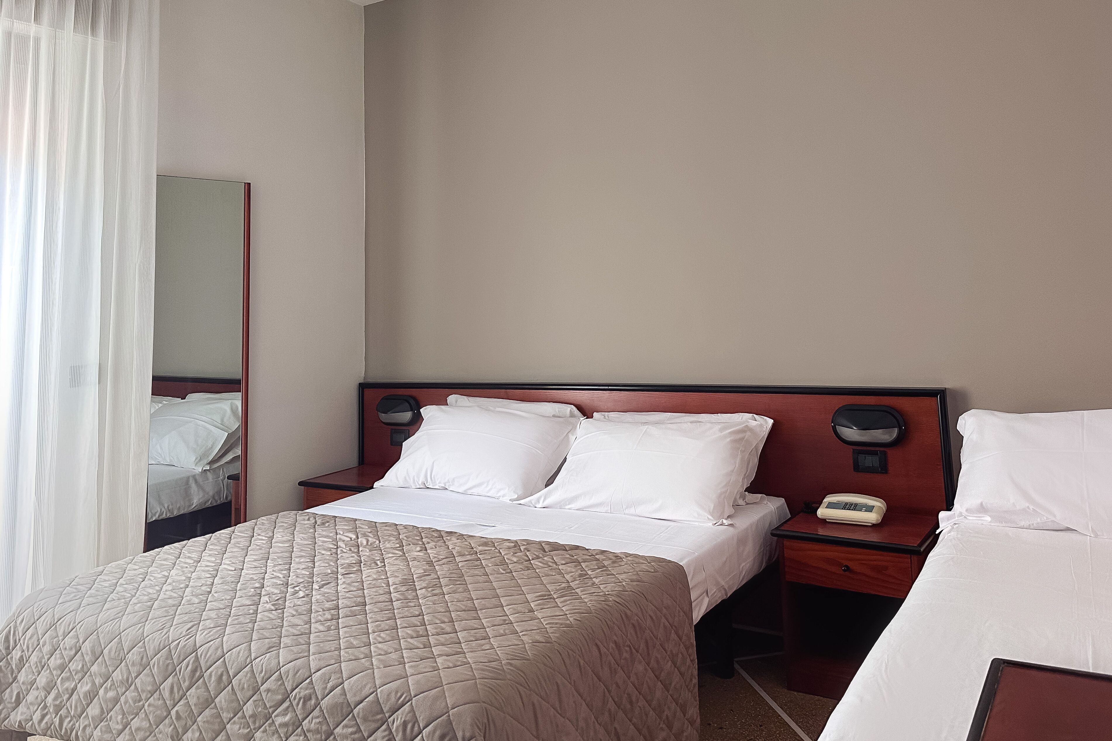 A hotel room with a large bed, two bedside tables, a bedside lamp, and a mirror on the wall.