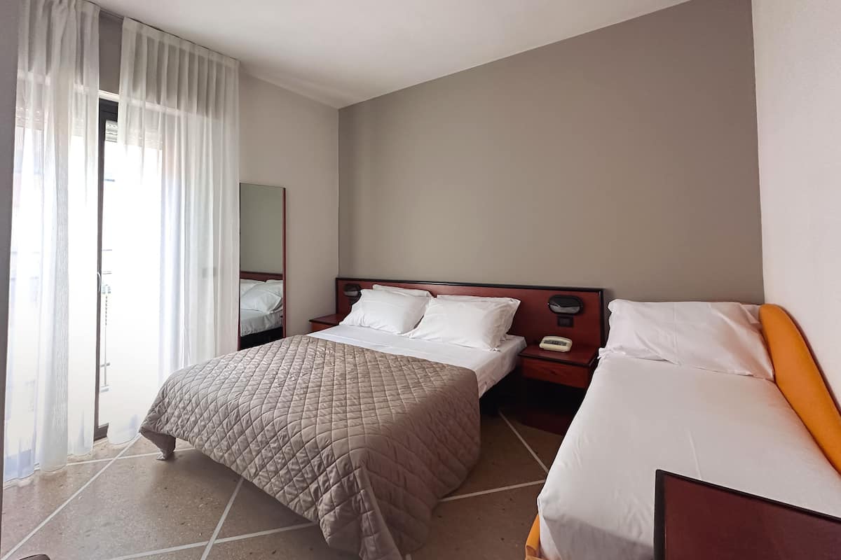 A hotel room with a queen-sized bed, a smaller bed, a nightstand with a phone, and a large window with sheer curtains.