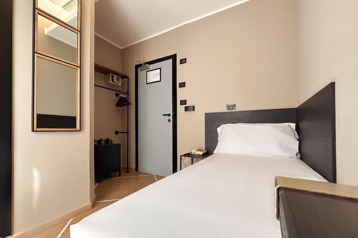 A hotel room with a bed, bedside table, and a mirror.
