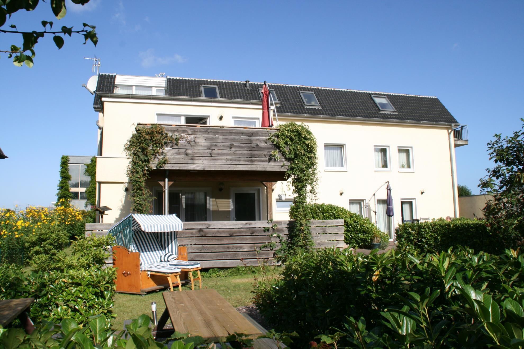 A two-story house with a wooden deck, a covered seating area, and a garden.