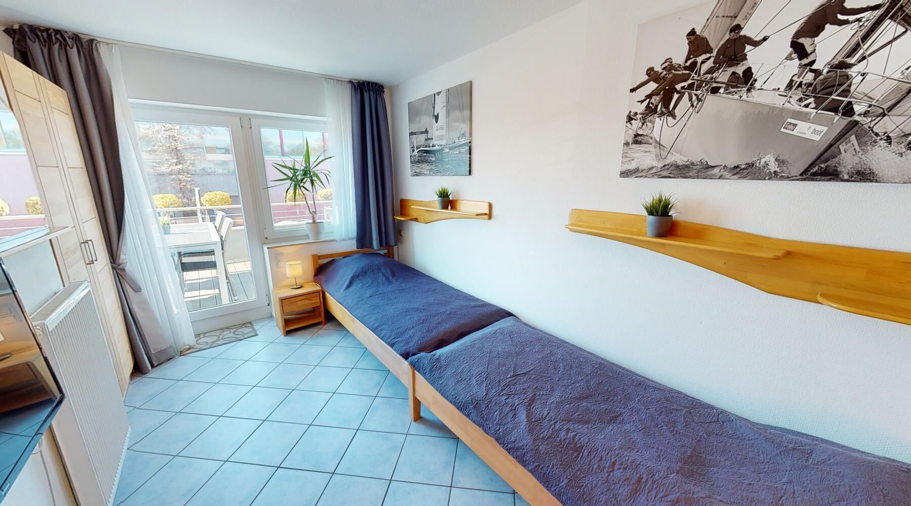 Ett litet, modernt rum med en säng, ett fönster med gardiner, ett litet bord med en lampa och en vägghylla med en växt.