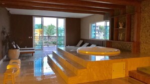 A modern bathroom with a large bathtub, a wooden ceiling, and a view of palm trees outside. - Golf Ville Resorts Suites (Aquiraz)