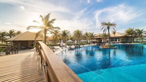 A resort pool area with palm trees, lounge chairs, and a wooden deck. - Golf Ville Resorts Suites (Aquiraz)