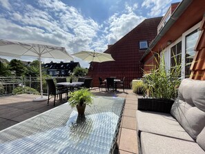 An outdoor patio with a glass table, chairs, and umbrellas. - Vacation apartment Parkpension W16 (Laboe)