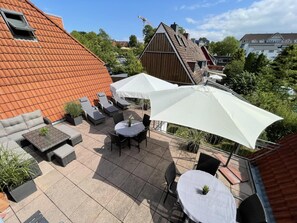 An outdoor patio area with seating and umbrellas, surrounded by buildings with red and brown roofs. - Vacation apartment Parkpension W16 (Laboe)