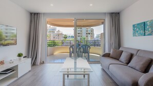 Una sala de estar moderna con una mesa de vidrio, sofá y un balcón con vistas a edificios.