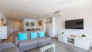 Una sala de estar moderna con un sofá, una mesa de centro de vidrio, un mueble blanco para entretenimiento y un televisor de pantalla plana.