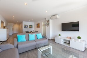 Una sala de estar moderna con un sofá, una mesa de centro de vidrio, un mueble blanco para entretenimiento y un televisor de pantalla plana.