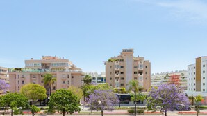 Un edificio residencial de varios pisos con balcones, rodeado de árboles y un cielo despejado.