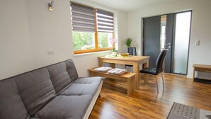 Una sala de estar moderna con un sofá gris, una mesa de comedor de madera con dos sillas, un pequeño banco y una planta en maceta.