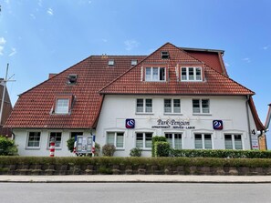 Ein zweistöckiges Gebäude mit rotem Ziegeldach und einem Schild mit der Aufschrift 'Park-Pension'.