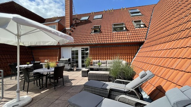 En patio med udendørs møbler, et overdækket siddeområde og udsigt til en bygning med rødt tegltag.