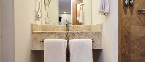 A bathroom with a marble countertop, two white towels, a hairdryer, and a mirror.