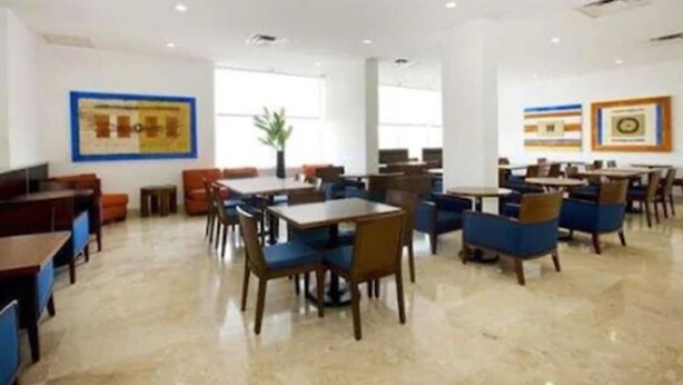 A spacious dining area with multiple tables and chairs, large windows, and framed artwork on the walls. - BH Business Hotel Group (Reynosa)