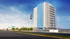 A tall hotel with a blue and white facade, a prominent 'B' sign, and a parking sign indicating 105 available spaces. - BH Business Hotel Group (Reynosa)