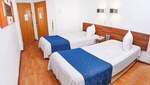A hotel room with two beds, wooden flooring, a wooden headboard, a bedside table with a phone, and a wall-mounted light fixture. - BH Business Hotel Group (Reynosa)
