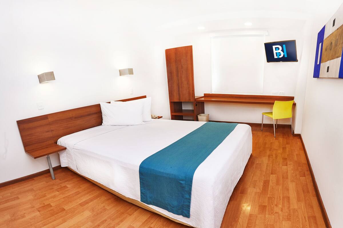 A hotel room with a bed, a desk, a chair, and a television.