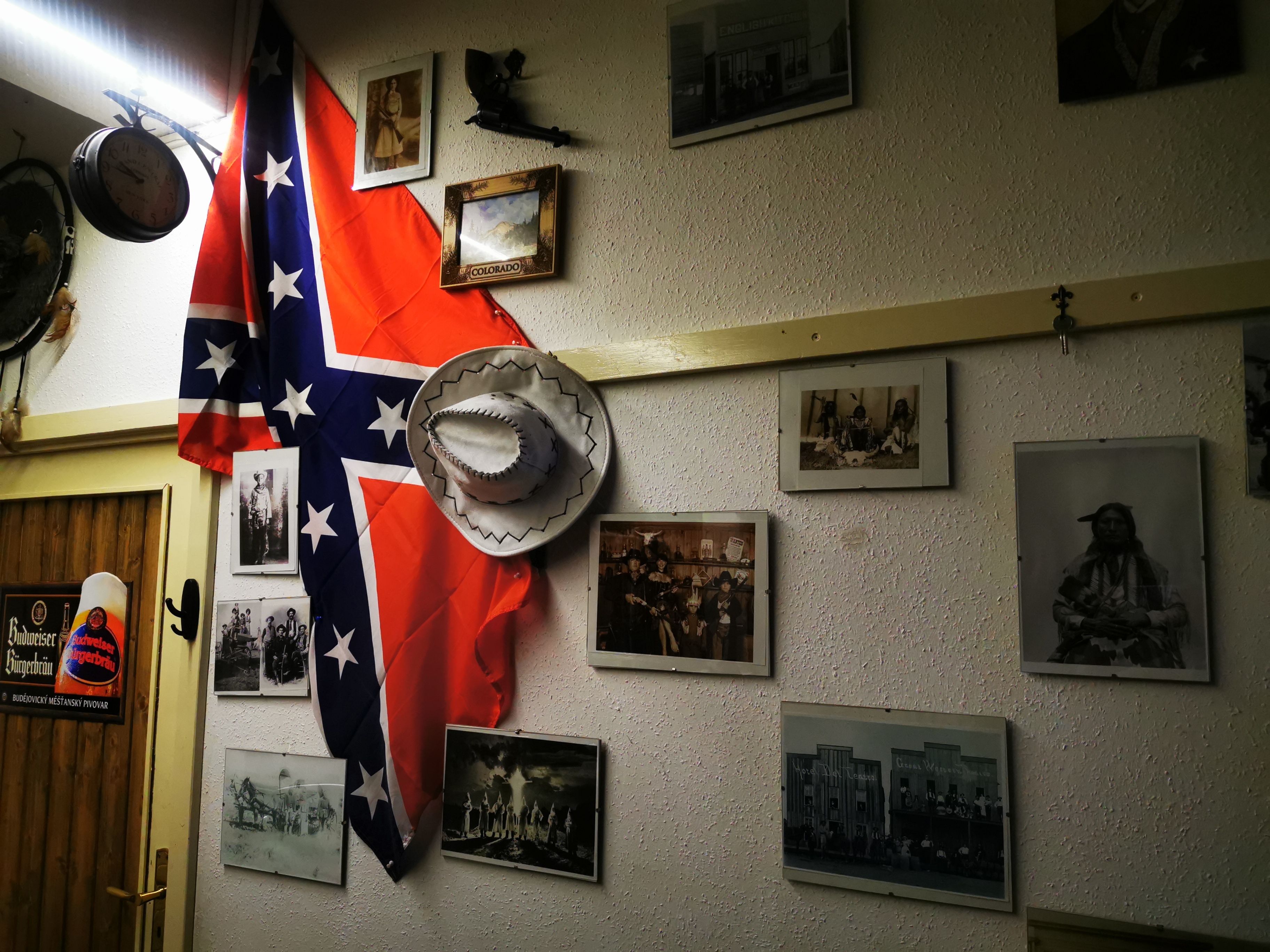 Una habitación con una pared decorada con diversas fotografías enmarcadas y una bandera grande.