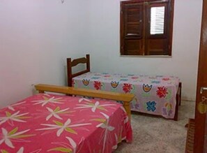 A small bedroom with a bed, a chair, and a table with a floral tablecloth. - Pousada Tia Cota (Barreirinhas)