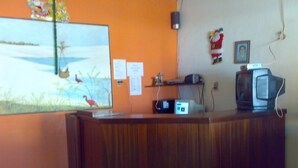 A reception desk with a computer monitor, a television, and a painting of birds on the wall. - Pousada Tia Cota (Barreirinhas)