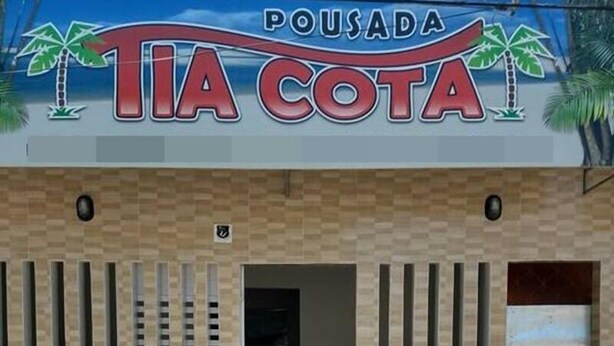 A building with a sign reading "Pousada Tia Cota" and palm trees on either side. - Pousada Tia Cota (Barreirinhas)