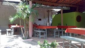 An outdoor patio area with tables and chairs, some covered with red tablecloths, and a few potted plants. - Pousada Tia Cota (Barreirinhas)