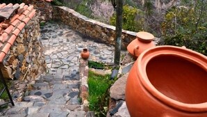 Ein steiniger Weg führt zu einem terrassierten Garten mit Terrakotta-Töpfen und einem großen Tonkrug.