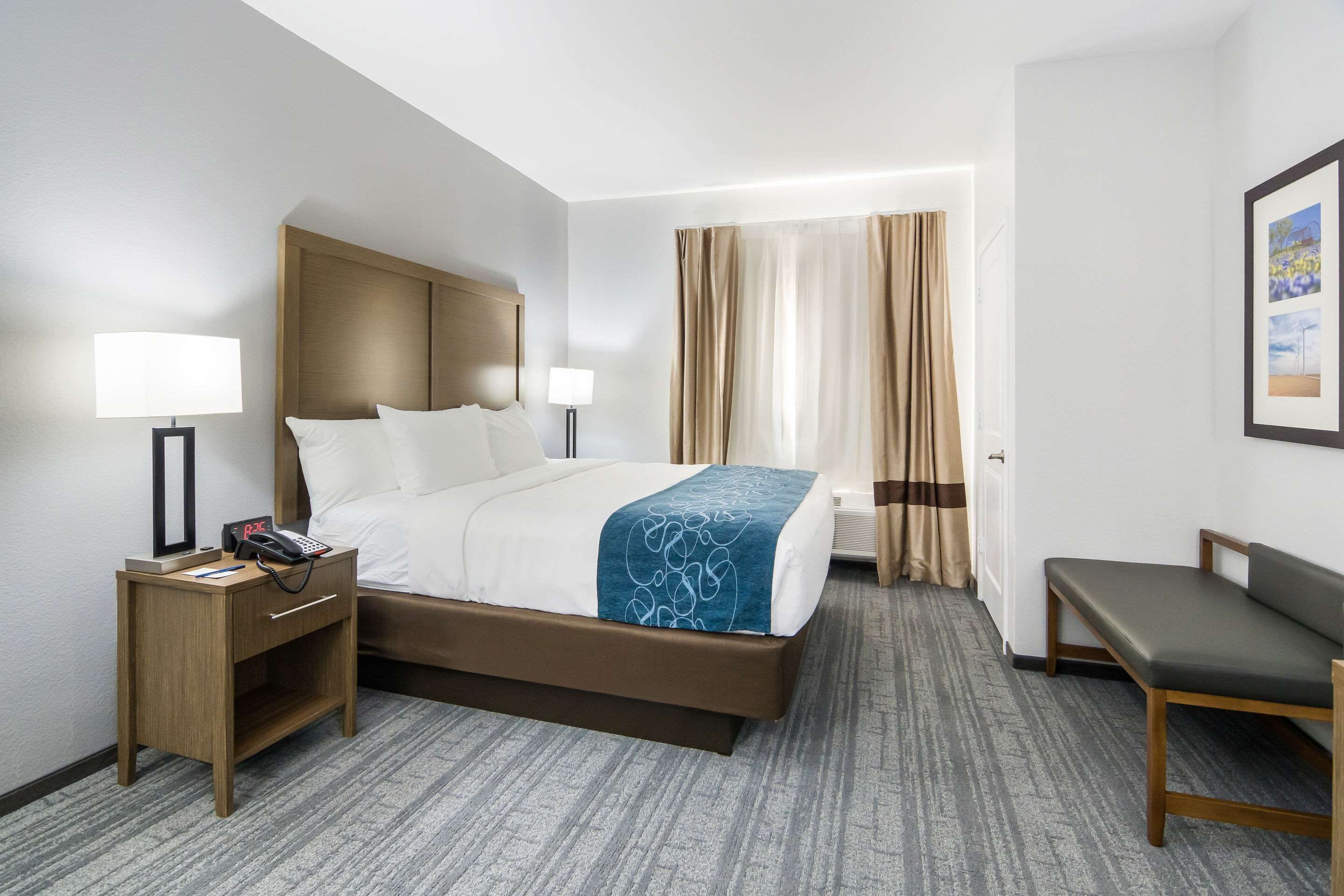 A hotel room with a bed, bedside tables, a desk, a chair, and a window with curtains.