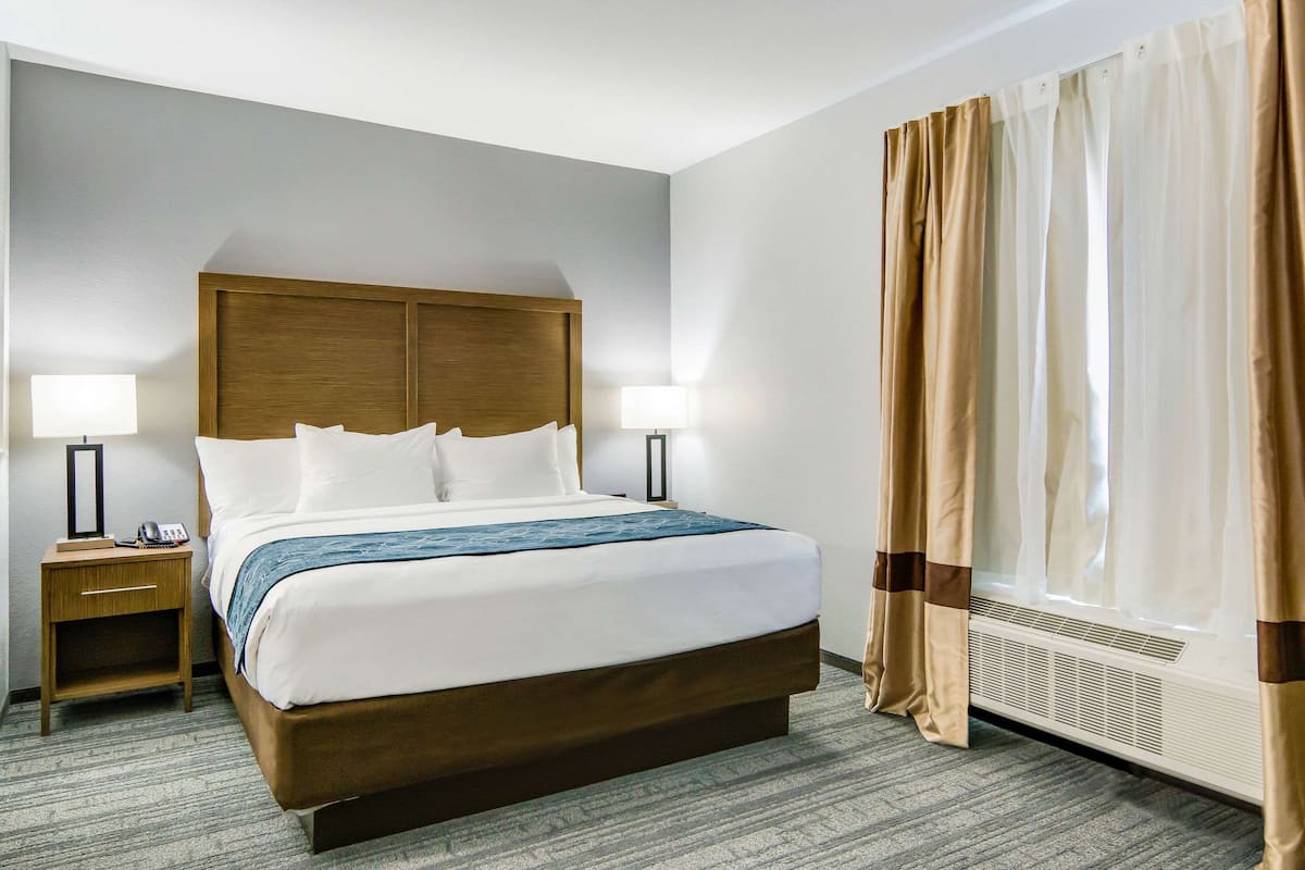 Habitación de hotel con una cama grande, dos mesitas de noche con lámparas, una ventana con cortinas y un calentador fijado a la pared.