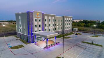 A modern hotel with a central entrance, multiple floors, and a parking lot.
