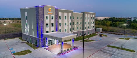 A modern hotel with a central entrance, multiple floors, and a parking lot.