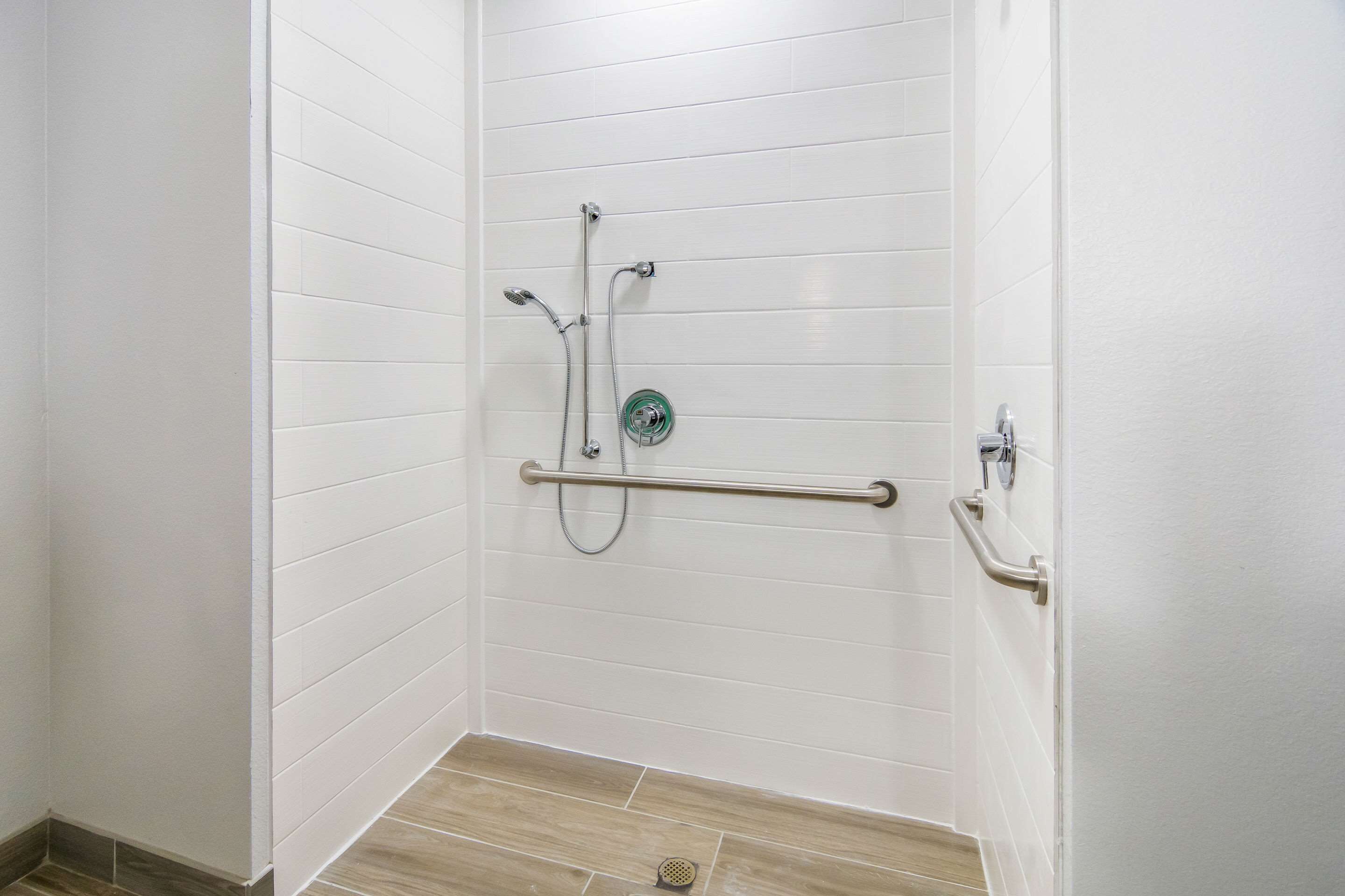 Zona de ducha con paredes de azulejos blancos, suelo de madera y barandilla.