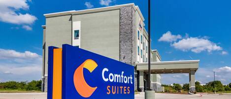 Een Comfort Suites hotelbordje met een modern gebouw op de achtergrond.