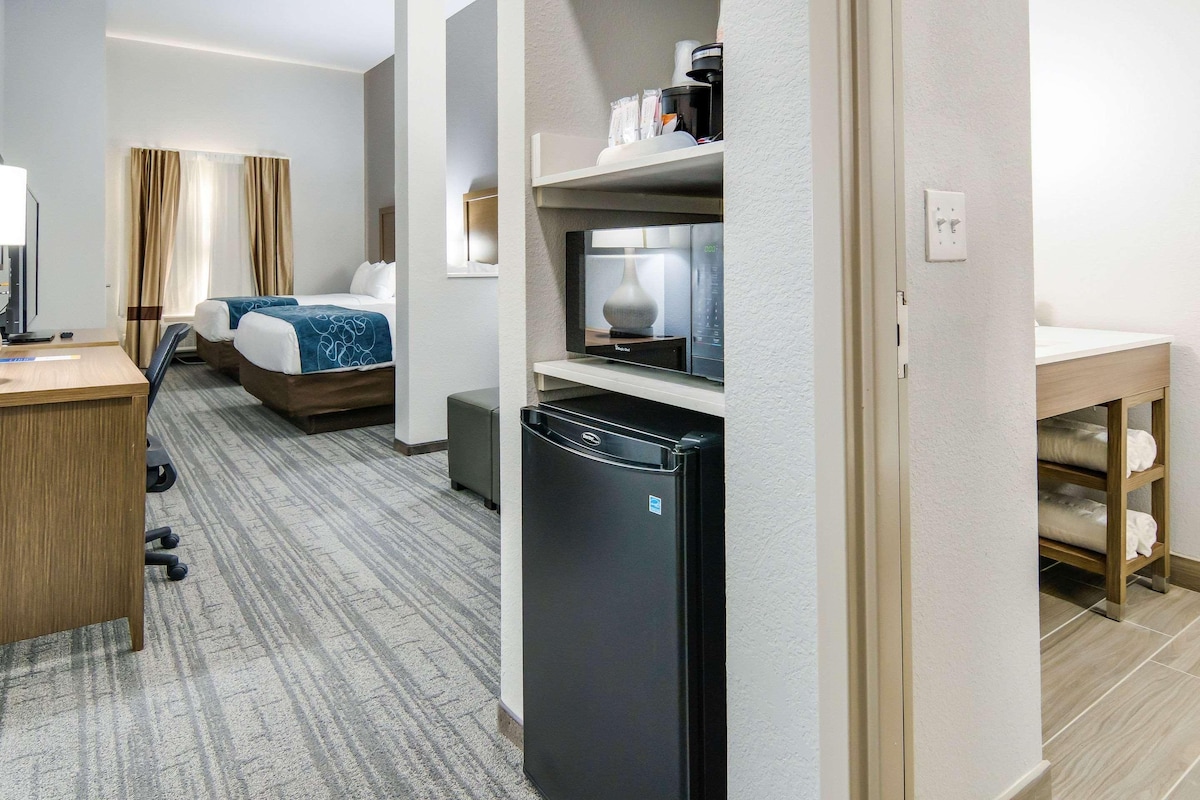 Une chambre d’hôtel équipée d’un lit, d’un bureau, d’un réfrigérateur, d’un four à micro-ondes et d’une petite table avec une lampe.