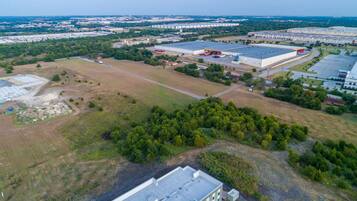 An industrial area with large warehouses, open fields, and scattered trees.