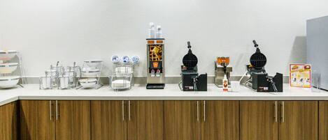 A kitchen counter with various appliances and utensils, including a coffee machine, a waffle maker, and a food processor.
